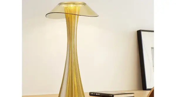 Elegancka, złota lampka stołowa o smukłej, prążkowanej podstawie i szerokim kloszu, tworząca ciepłe światło.