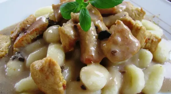 Pyszne gnocchi z kurczakiem w sosie śmietanowym, udekorowane listkiem bazylii. Danie wygląda apetycznie i sycąco.