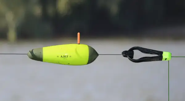 Gelber Wels-Schwimmer mit orangefarbenem Antennenstift und schwarzem Clip an einer Angelschnur.