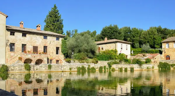 Antica sorgente termale con edifici in pietra e riflessi sull'acqua, un incantevole scorcio dei borghi del Val d'Orcia.