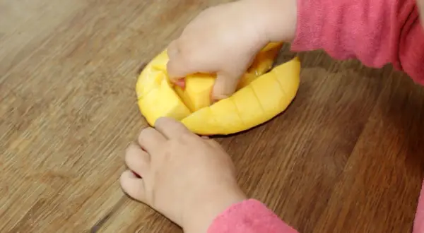 Kleine Hände erkunden eine aufgeschnittene Mango. Ab wann darf ein Baby Mango essen?