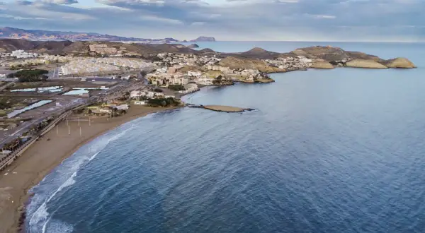 Vista aérea de la costa de Pulpí, con su extensa playa de arena dorada y el mar azul. El pueblo se extiende por la ladera de las colinas.
