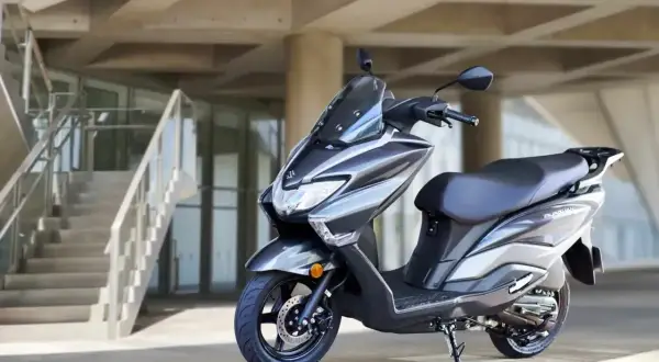 Szary skuter Suzuki Burgman, znany jako jeden z najbardziej bezawaryjnych skuterów, zaparkowany przed nowoczesnym budynkiem z betonowymi schodami.