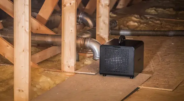 Svart avfuktare krypgrund placerad bland träbjälkar och isolering, med ventilationsrör i bakgrunden.