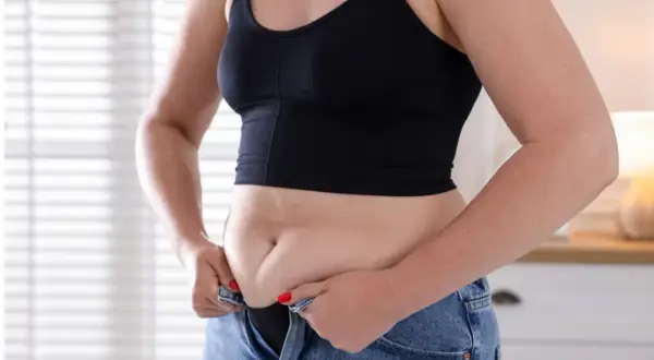 Frau kämpft mit dem Hosenknopf, um den hormonbauch loszuwerden.