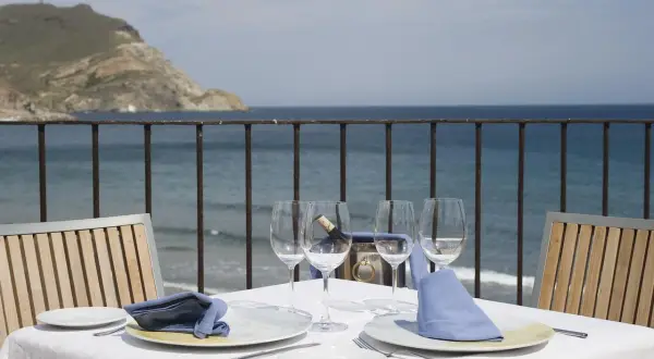Mesa puesta en Doña Pakyta restaurante con vistas al mar. Copas, platos y servilletas azules esperan a los comensales.