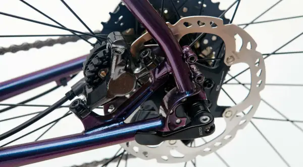 Błyszcząca, fioletowa rama roweru z widoczną sztywną osią w rowerze, hamulcem tarczowym Shimano i kasetą.