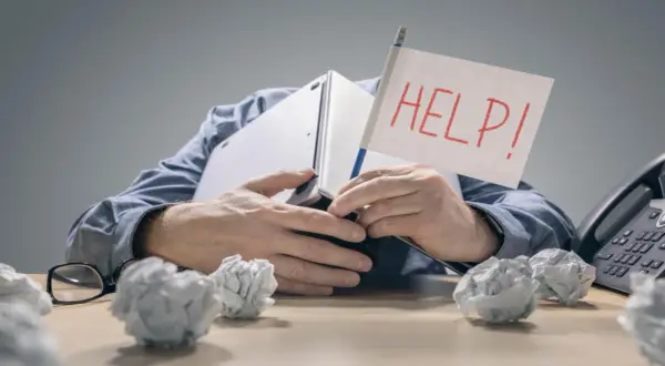 Zestresowany mężczyzna pod laptopem z flagą "HELP!" zastanawia się, ile wzrosną raty kredytów. Wokół niego papierowe kule.