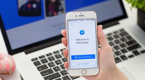 Dłoń trzyma iPhone'a z ekranem powitalnym Messengera. Dowiedz się, jak ustawić dymki czatu Messenger na iPhone.