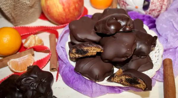 Pyszne pierniczki w czekoladzie, z widocznym nadzieniem, otoczone mandarynkami, jabłkiem i laskami cynamonu.