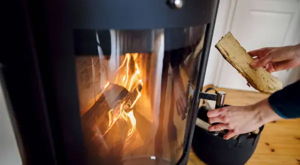 Hände legen Bauholz in einen brennenden Kamin, um Wärme zu erzeugen.