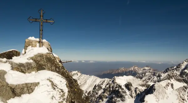 Szczyt Gerlach bez przewodnika. Krzyż na skalistym, ośnieżonym wierzchołku, w tle zimowe Tatry i błękitne niebo.