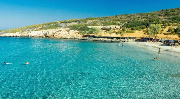 En solig strand med turkost vatten och människor som badar. En perfekt dag att se på Kreta.
