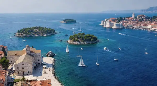 Un día perfecto para tu ruta Croacia 7 días: veleros navegan en aguas turquesas cerca de islas verdes y la histórica ciudad amurallada.
