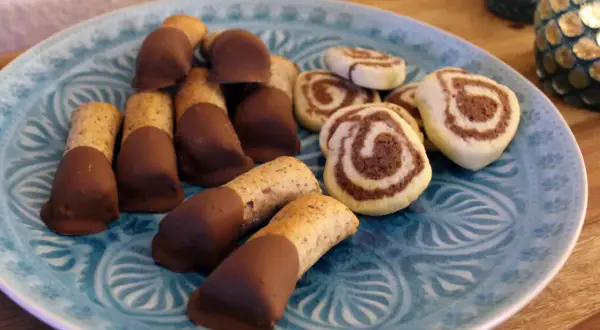Mandelstangen mit Marzipan und schokoladenüberzogenen Keksen auf blauem Teller.