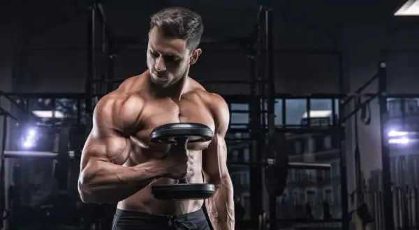 Uomo muscoloso in palestra con manubrio, focus sulla definizione muscolare, integrando la creatina per massimizzare i risultati.