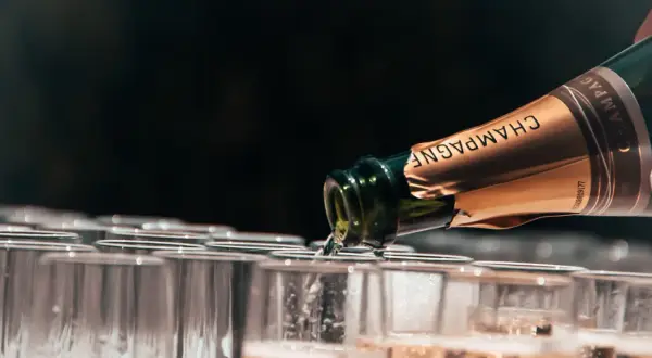 Versando champagne da una bottiglia in una fila di bicchieri, mostrando diversi tipi di champagne.