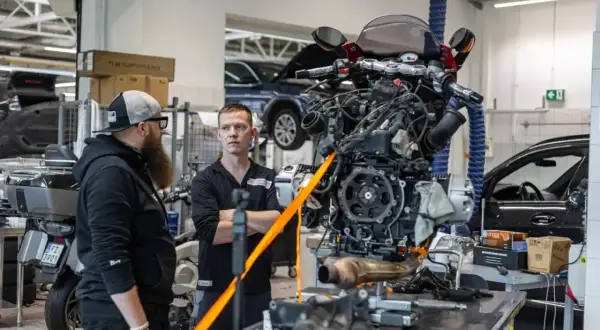 Mechanicy omawiają regulację linki sprzęgła przy silniku motocykla wiszącym na taśmach.