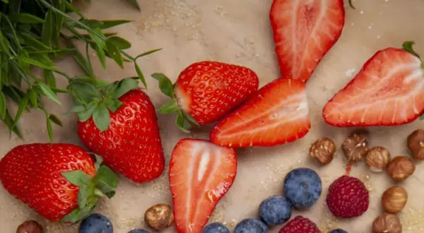Frische Erdbeeren, Blaubeeren und Himbeeren liegen bereit, um sie einzufrieren. Ein paar Haselnüsse und grünes Blattwerk runden das Bild ab.