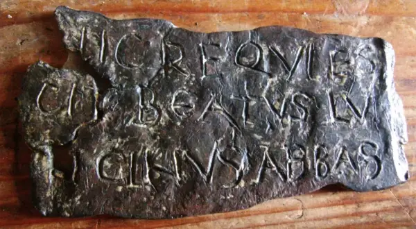 Plaque de métal gravée de lettres latines, possiblement une inscription trouvée près de la tour de Saint-Lupicin.