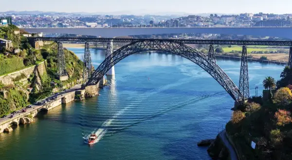 Majestatyczny porto most nad błękitną rzeką, z łodzią przecinającą fale i miastem w tle.
