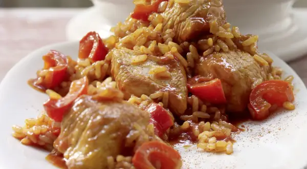 Serbisches Reisfleisch mit zarten Fleischstücken und Tomaten, serviert auf einem weißen Teller.