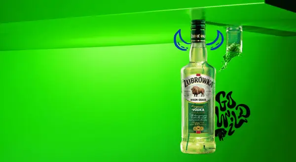 Butelka Żubrówki z trawą żubrową, 37,5% alkoholu. Obok kieliszek z zielonym płynem i napis "Go Wild".