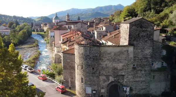 Antica porta in pietra lungo la via del Volto Santo, con fiume e case arroccate sui monti.