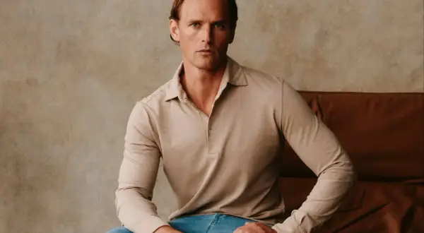 Ein Mann sitzt lässig in einem beigen Langarm-Polohemd, das an italienische Poloshirts für Herren erinnert.
