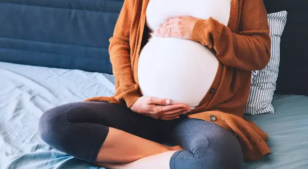 Mujer embarazada sentada, con las manos sobre su vientre. Ejercicios para el embarazo y alivio de la pubalgia.