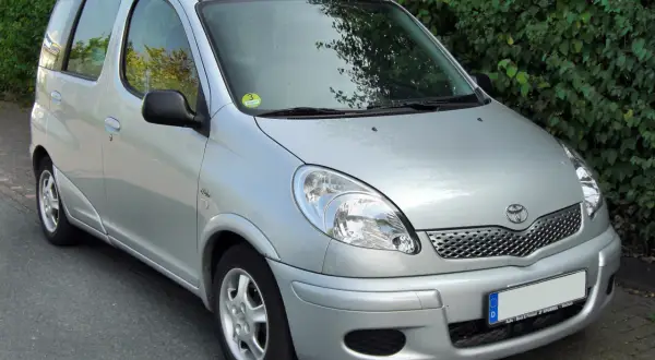 Srebrny Toyota Yaris Verso zaparkowany przy żywopłocie.