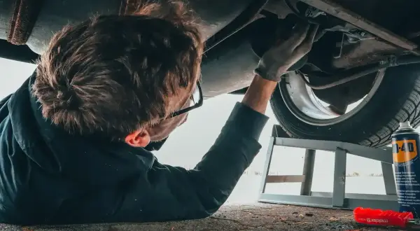 Mechanik pod samochodem, zastanawia się ile zarabia diagnosta samochodowy.