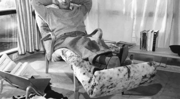 Man vilar i en Bruno Mathsson liggfåtölj, klädd i fårskinn. Böcker och tidningar ligger utspridda.