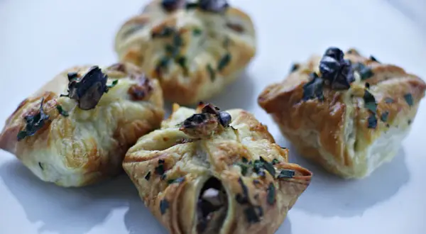 Cztery apetyczne paczuszki z ciasta francuskiego z gruszkami i gorgonzolą, posypane ziołami.