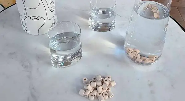 Des perles de céramique dans une carafe d'eau pour purifier l'eau du robinet naturellement. Des verres d'eau et un pichet décoratif complètent la scène.