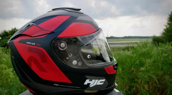 Czerwono-czarny kask motocyklowy HJC RPHA 70 z przyciemnianą blendą, gotowy na podróż pośród zieleni.