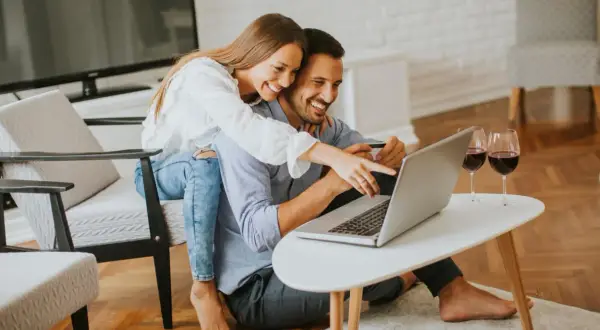 Szczęśliwa para robi zakupy online, ciesząc się ulgą na internet i lampką wina.