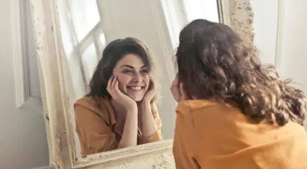 Donna sorride guardandosi allo specchio, un momento di riflessione sull'effetto specchio psicologia e sull'accettazione di sé.