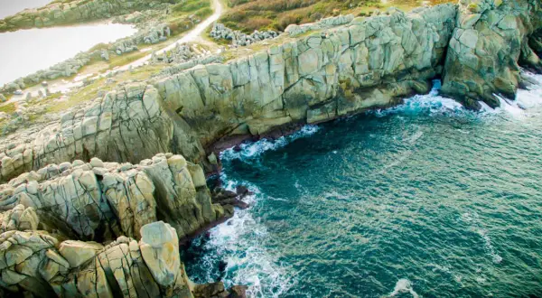 Impresionantes acantilados galicia, con el mar azul turquesa rompiendo contra las rocas. Senderos serpentean por la vegetación verde.