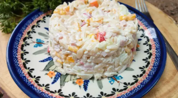Pyszna sałatka z makaronem orzo, szynką i ogórkiem, podana na ozdobnym talerzu.
