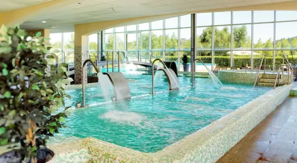 Piscina interior con cascadas de agua y vistas al exterior, ideal para una experiencia de spa relajante.