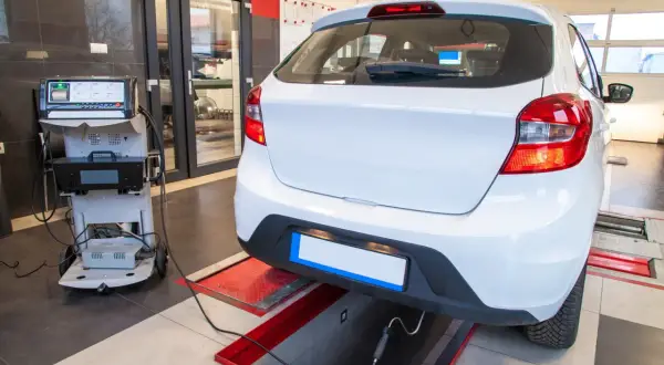 Controllo emissioni per la revisione microcar. Un'auto bianca è collegata a un analizzatore di gas di scarico in un'officina.