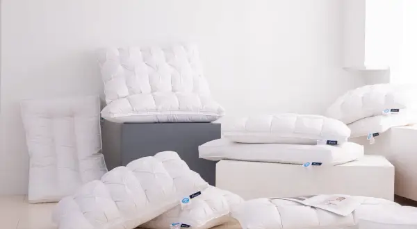 A pile of fluffy white down pillows, some with tufted patterns. One new down pillow smells bad, but the others look inviting.