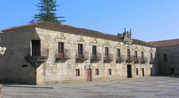 El Pazo de Fefiñanes, un edificio de piedra con balcones de hierro forjado, se alza bajo un cielo azul.