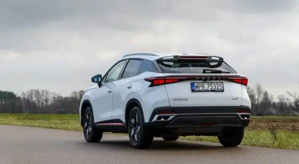 Białe, nowoczesne chinskie auto OMODA 5 z charakterystycznym pasem świateł z tyłu, zaparkowane na poboczu drogi.