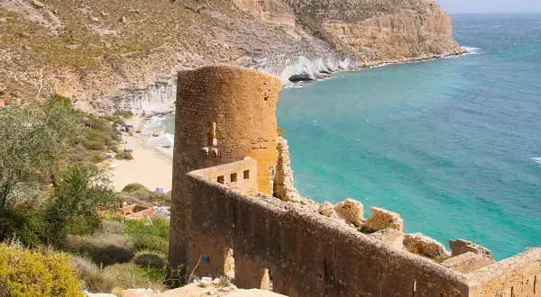 Ruinas de un antiguo torreón y murallas de piedra junto a una cala de aguas turquesas. Un lugar con historia que ver en Las Negras, Almería.