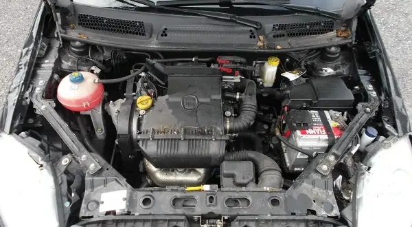 Silnik w fiat bravo 2011, widok z góry. Widać akumulator, zbiornik płynu chłodniczego i elementy silnika.