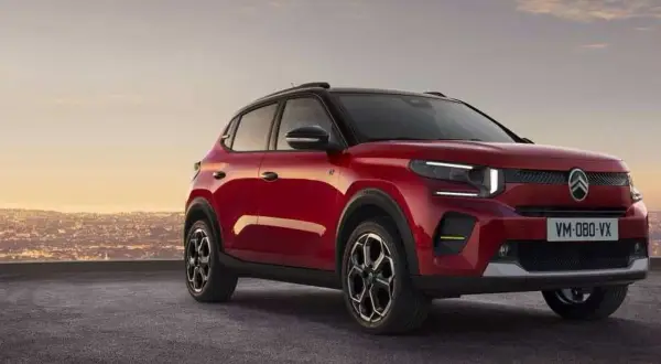 Nowy, czerwony Citroen C3 2025 z czarnym dachem i felgami, zaparkowany na tle miasta o zachodzie słońca.