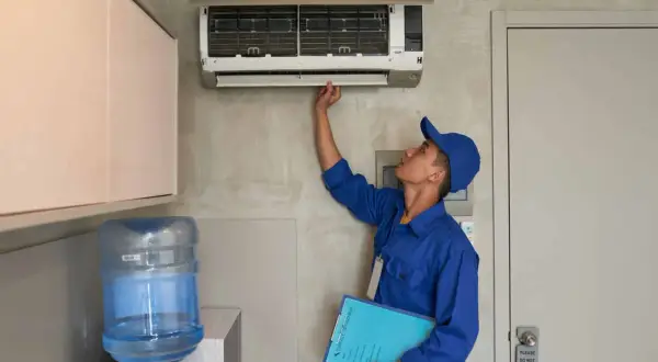 Un technicien en uniforme bleu vérifie une installation de climatisation murale, tenant un dossier de service.