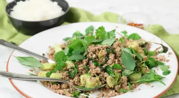 En tallrik med kycklingfärs, färska örter och grönsaker, perfekt för ett snabbt larb recept. Ris i bakgrunden.